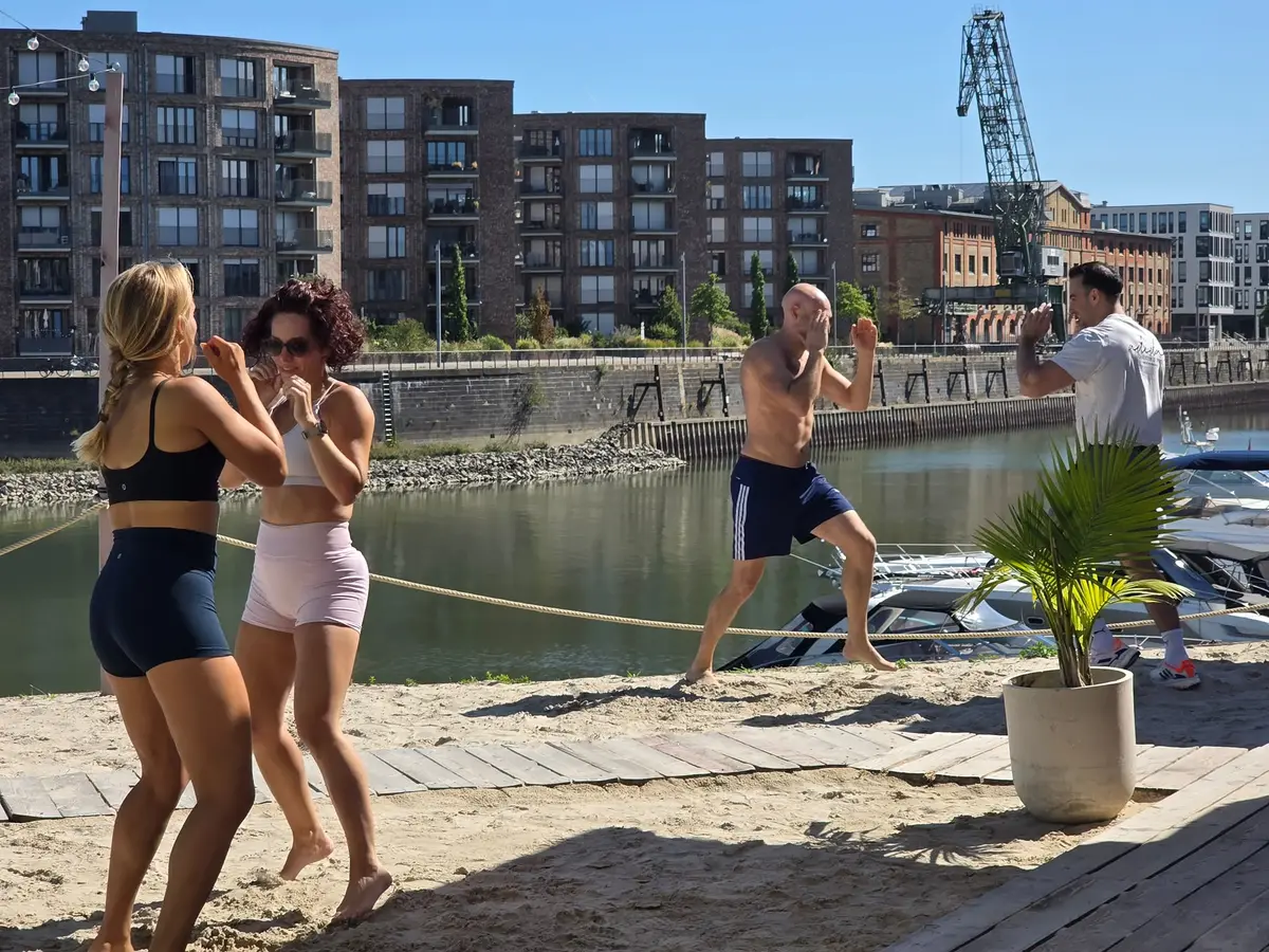 Teilnehmerinnen und Teilnehmer üben Schläge am Sandstrand am Zollhafen